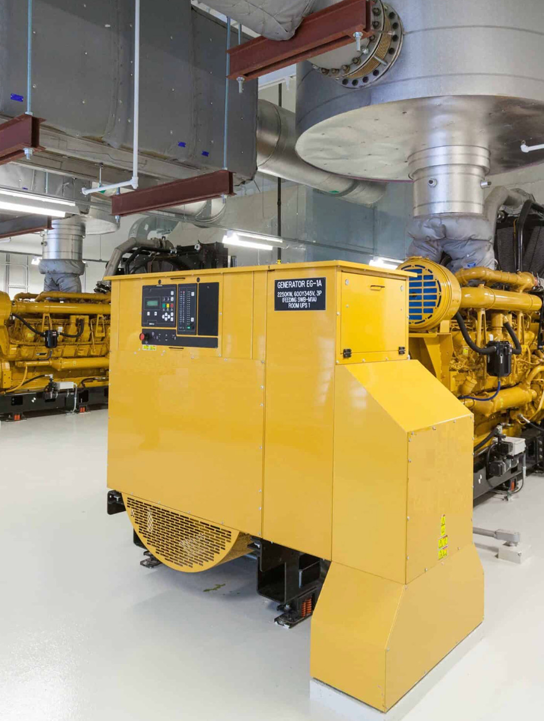 Yellow gas generator set with exhaust ducting inside a plant room